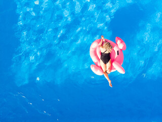 Happy woman on flamingo pool float in pool, drone aerial view. Summer holidays