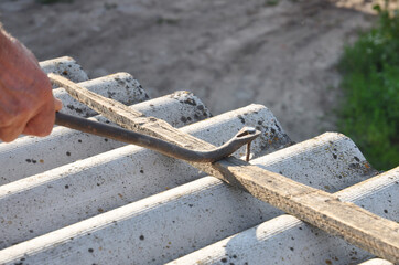 Roofer removes a nail from an asbestos roof sheet on the house rooftop