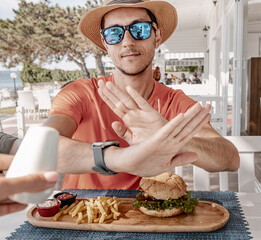 Young man wearing sunglasses and a hat, rejecting salt while enjoying lunch at a seaside...