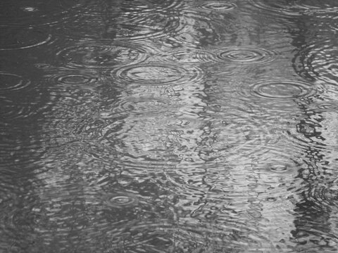A black and white photograph of raindrops falling onto the surface of a puddle of water.
