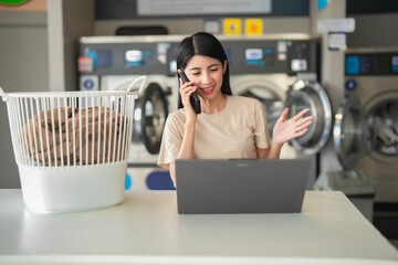 Young female freelancer making a phone call and working at a laundromat. Modern multitasking lifestyle, communication, and tech.