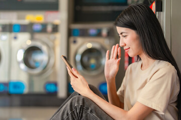 Asian woman waving at her smartphone during a video call. Friendly gesture, virtual communication, online meeting from home or casual environment.