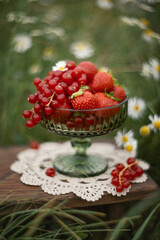 A photo of strawberries and red currants in a vase.