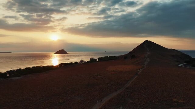 Aerial view of rolling hills meeting the ocean, with small islands and golden sunlight reflecting on the water, Poto Tano, Indonesia.