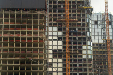 Obraz premium Dynamic urban construction site featuring multiple modern skyscrapers in various stages of construction with exposed concrete frameworks, reflective glass facades and towering yellow cranes