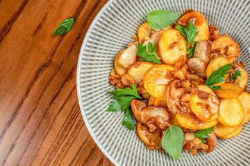 Crispy golden potato slices garnished with herbs and caramelized onions are served in a patterned ceramic bowl on a wooden table. top view. copy space