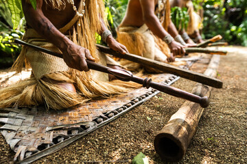 Hands of warriors from Futuna, Vanuatu, beat a bamboo log in time during a customary dance. Dressed in woven pandanus attire, they celebrate their cultural heritage.
