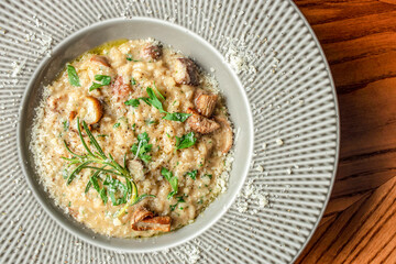 Creamy mushroom risotto garnished with fresh herbs and parmesan cheese is served in a wide-rimmed ceramic bowl on a wooden table top view. copy space