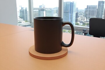 Black mug on a light brown coaster on a light orange table, overlooking a city skyline through large windows
