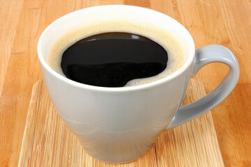 Grey mug of dark coffee on wooden surface