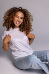 Curly Woman Sitting On Floor In White T-Shirt And Blue Jeans