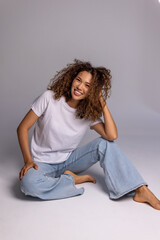 Curly Woman Sitting On Floor In White T-Shirt And Blue Jeans