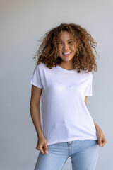 Beautiful Curly Woman Posing In White T-Shirt And Blue Jeans On Gray Background