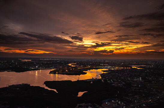 Aerial view of the city's waterways reflecting the fiery sunset sky, creating a mesmerizing contrast between the dark silhouettes of buildings and the shimmering water, Dakar, Senegal.