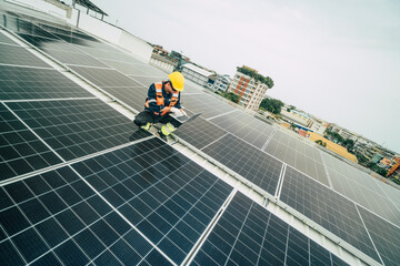 Technician inspects solar panels on rooftop in urban area during overcast afternoon