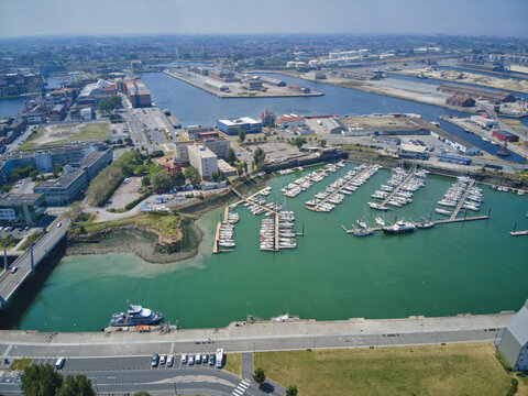 Aerial view of a vibrant harbor dotted with white yachts against the backdrop of industrial buildings and open skies, Dunkirk, France.