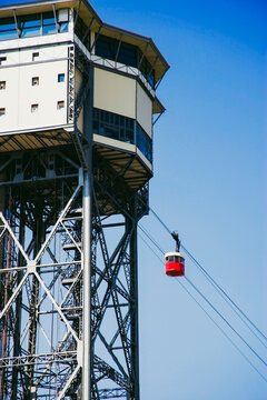 Urban detail of red cable car tower and elevator shaft with blue background, Barcelona, Spain, symbol of city infrastructure and mobility.