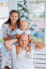 Family portrait in a bright indoor setting with a child on father's shoulders