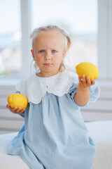 Young child holding lemons indoors with sunlight streaming through the window