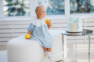Little girl in blue dress enjoys lemons beside elegant cake in bright room