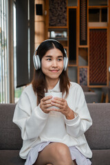 A young woman enjoys a peaceful moment with headphones and a cup of coffee in a stylish, modern living room.