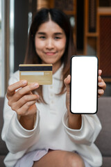 Smiling woman holding a credit card and smartphone with a blank screen, ideal for online shopping or mobile payment themes.