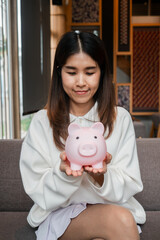 Young woman in casual attire holding a pink piggy bank, symbolizing savings and financial planning.