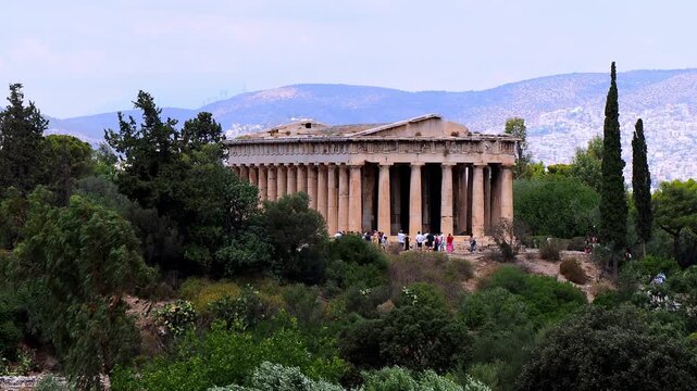 View of the Temple of Hephaestus at the foot of Acropolis Hill in Athens, Greece, surrounded by greenery and ancient ruins.