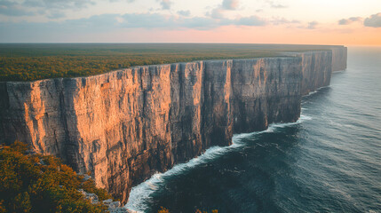 Aerial view of a cliff face meeting the ocean at sunset