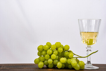 Racimo de uvas verdes  con una copa de vino blanco al lado con fondo blanco 