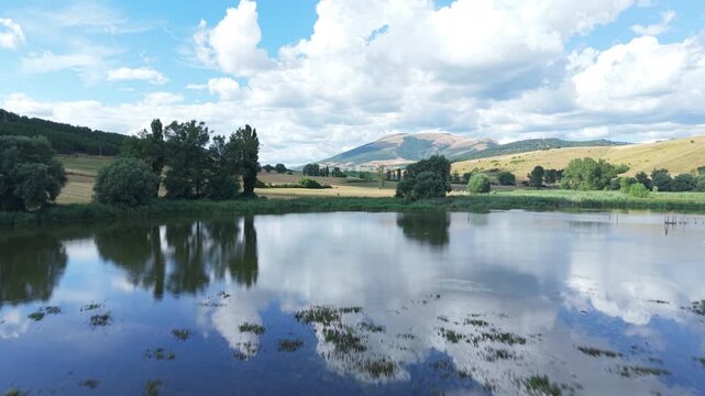 A stunning aerial 4K shot of Lago di Colfiorito surrounded by lush summer landscape in Umbria, Italy. The footage showcases the tranquil water, green countryside, and natural beauty.