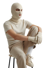 Stylish Minimalist Man In Monochrome Cream Knit Sweater And Trousers With Tactical Balaclava Seated On Modern Stool Isolated On PNG Background.
