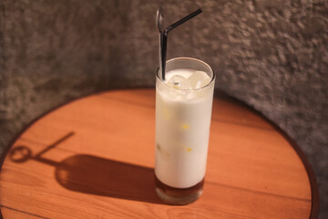 a glass of white milk with ice and a straw on a table with an unfinished wall in the background.