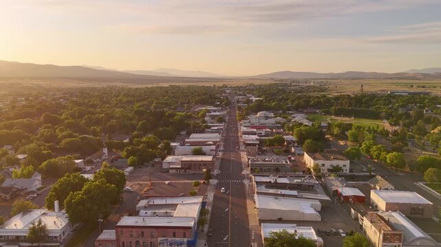 Susanville, United States, aerial view of the main street lined with buildings, trees, and mountains bathed in the golden light of the early morning sun.