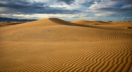 Expansive sand dunes under a cloudy sky with ripples in the sand at sunset