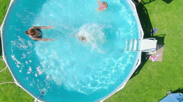 Top-down aerial shot. A happy young girl jumps into a blue frame pool in a backyard on a sunny day. A perfect concept for summer vacation, family fun, and happy childhood memories