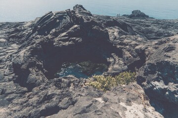Dark volcanic rocks form a cliff overlooking a small pool of water