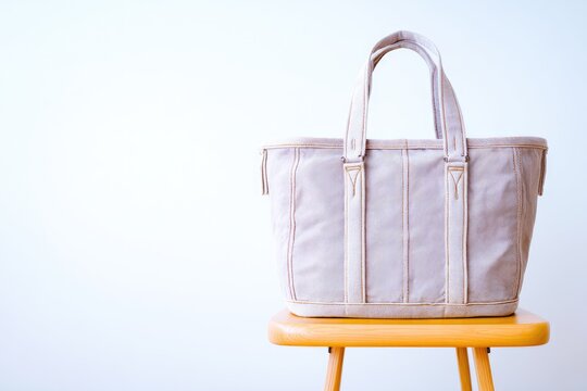 Light mauve tote bag on a wooden stool against a white wall - Powered by Adobe