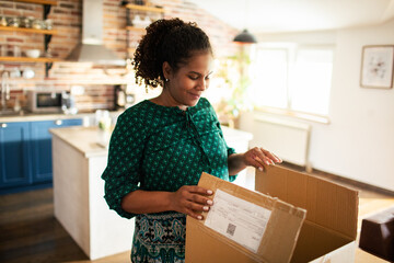 Happy woman opening package box in cozy home kitchen