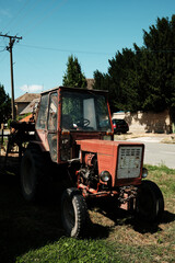 Naklejka premium Old red tractor with a trailer parked on grass in a residential street in Apatin, Serbia, on a sunny day.