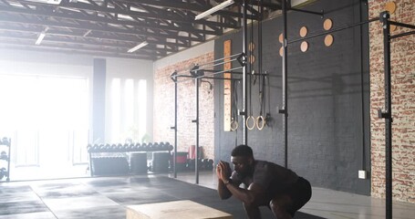 African American male executing plyometric box jumps from squat for explosive strength on gym floor - Powered by Adobe