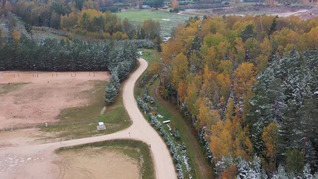 A drone flies over Ogres Zilie Kalni in Latvia, revealing the quarry parking area bordered by autumn forests with snow-dusted, colorful trees for a vibrant seasonal view.
