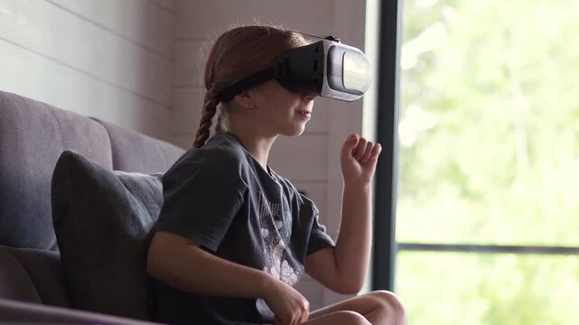 Amazingly surprised Caucasian girl child schoolgirl is playing an online video game in a 3D world using virtual reality. Explore cyberspace with VR glasses. Virtual boxing, wrestling