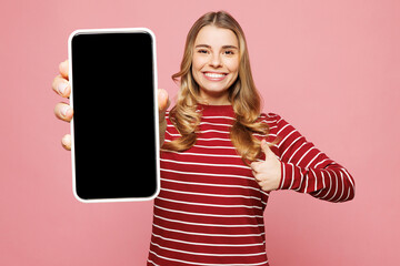 Fototapeta premium Young woman she wearing red striped sweatshirt casual clothes holding in hand use mobile cell phone with blank screen workspace area show thumb up isolated on plain pink background. Lifestyle concept.