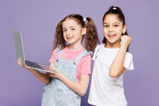Little happy two friends kids children IT girls 9-10 years old wear casual clothes together hold use work on laptop pc computer do winner gesture isolated on plain purple background Lifestyle concept