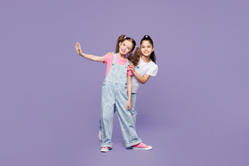 Full body smiling fun little two friends kids children girls 9-10 years old wearing casual clothes together posing hug raise up hand look camera isolated on plain purple background. Lifestyle concept.