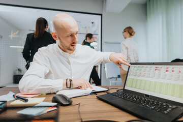 Business team analyzing financial data together in an office. A close-up view shows one member engaging in a discussion while pointing at a laptop screen displaying spreadsheets.