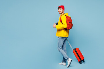 Traveler man he wear hat yellow casual clothes hold bag show thumb up isolated on plain pastel blue...