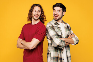 Young smiling happy two friends buddies men they wear casual clothes together stand back to back look to each other isolated on plain yellow orange color background studio portrait. Lifestyle concept.