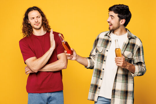 Young strict sober happy two friends buddies men they wearing casual clothes together hold give bottle of beer refuse to take and drink isolated on plain yellow orange background. Lifestyle concept.
